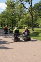 Group Of Disabled Women Driving Their Motorized Wheelchairs By The Road In Green Park