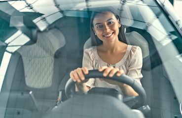 Young beautiful woman is choosing a new vehicle in car dealership. Lady in a car salon. Woman buying the car.