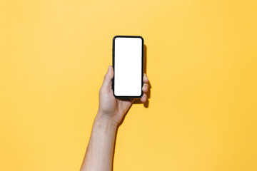 Wall Mural - Close-up of male hand holding smartphone with empty white mockup, isolated on yellow background.