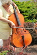 Female cellist with her instrument outdoors.