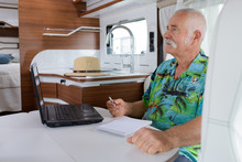 Senior Man Sat In Motorhome With Laptop And Notepad