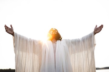 Wall Mural - Jesus Christ with his hands open and towards the sky with the sun shining in the background