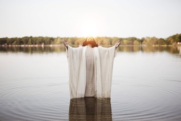 Jesus Christ standing in the water with his hands and head towards the sky