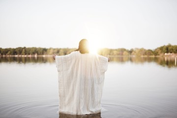 Wall Mural - Jesus Christ standing in the water with his hands up and the sun shining near his head