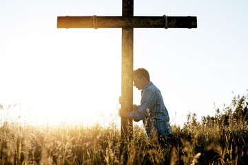Wall Mural - Male with his head leaned against a hand made wooden cross while praying