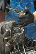 Mechanik w gumowych ochronnych czarnych rękawiczkach odkręca śruby kluczem nasadowym w skrzyni biegów. Odkręcanie obudowy skrzyni biegów.