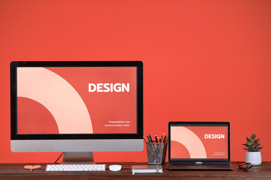 Designers workplace with two computer screens at wooden desk over coral background, copy space