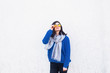 © alexaphotoua - Young brunette woman in Classic blue sweater and yellow glasses standing near white wall.