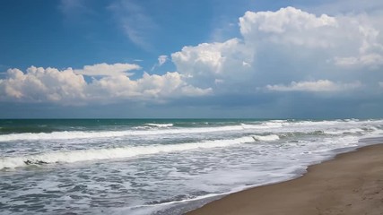 Wall Mural - ocean waves break on a sandy beach under a cloudy blue sky over a calm sea in this seamlessly loopin