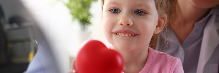 Little baby girl visiting doctor holding in hands red toy heart