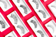 Different false eyelashes on a trendy red background. Beauty pop art pattern. Makeup accessories. Cosmetics products for women. Bright colorful backdrop. Closeup. Flat lay. Nobody