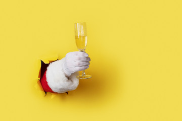Santa Holding Champagne Flute isolated over light yellow. Hand and arm only