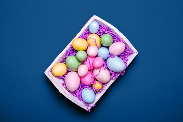 Wall Mural - Multicolor eggs in a white tray. Creative Easter concept. Modern solid classic blue background. Horizontal