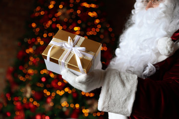 Poster - Santa Claus holding Christmas gift against blurred festive lights, closeup