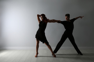 Beautiful young couple dancing near light wall