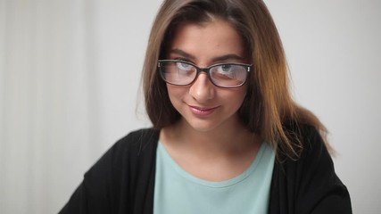 Wall Mural - Portrait of indian beautiful female student with glasses. Close-up of a young smiling woman. The face of a friendly girl writing in a notebook and looking at the camera.