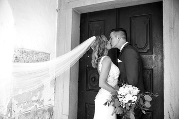 Wall Mural - The Kiss. Bride and groom kisses tenderly in front of church portal. Close up portrait of sexy stylish wedding couple kissing. Black and white photo.