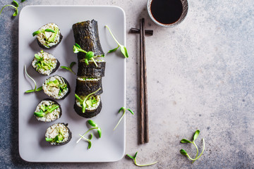 Vegan sushi rolls with avocado, brown rice, cucumber, tofu and seedlings on gray background, copy space. Plant based diet concept.