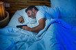 © TheVisualsYouNeed - night portrait of young stressed and paranoid American man in bed sleeping and holding gun fearing intruder breaking in home in paranoia and self defense concept