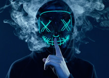 Anonymous Man Hiding His Face Behind Neon Mask In A Colored Smoke