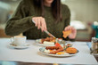 © chika_milan - Close up of caucasian woman in sweater sitting in restaurant and having french toast for breakfast.