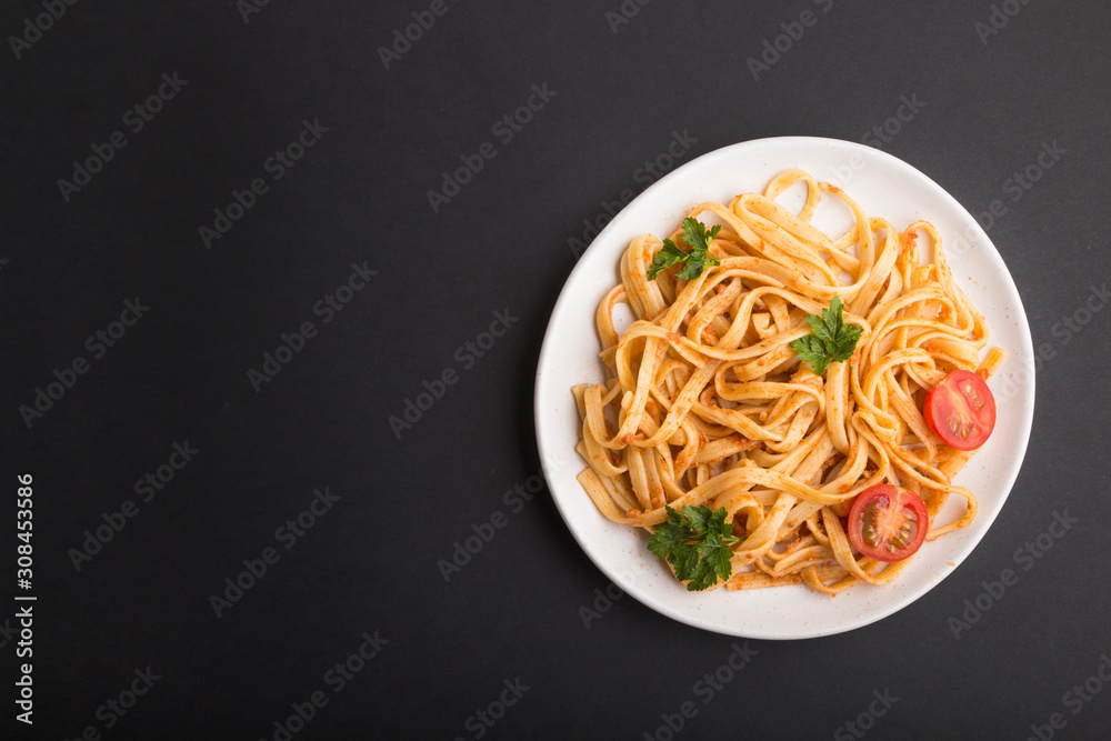 Semolina pasta with tomato pesto sauce, orange and herbs on a black background. Top view, copy space.