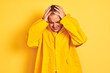 Young man wearing rain coat standing over isolated yellow background suffering from headache desperate and stressed because pain and migraine. Hands on head.