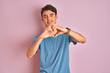 © Krakenimages.com - Teenager boy wearing casual t-shirt standing over blue isolated background smiling in love showing heart symbol and shape with hands. Romantic concept.