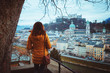 Young woman tourist stands with her back and enjoys the panoramic view of the medieval city of Salzburg.Very beautiful view of the winter Salzburg, the cathedral and the Hohensalzburg fortress Austria