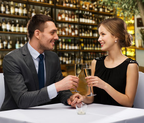 Poster - leisure and luxury concept - smiling couple clinking glasses of champagne over restaurant or wine bar background