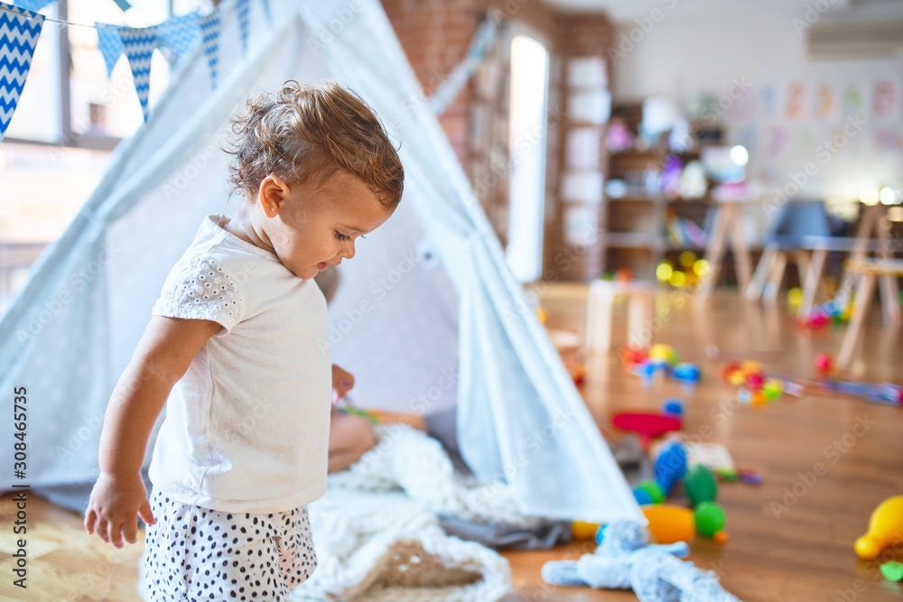 Adorable toddler playing around lots of toys at kindergarten