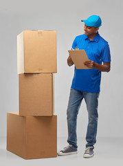 Poster - mail service and shipment concept - happy indian delivery man with boxes and clipboard in blue uniform over grey background