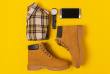 Layout Of Autumn Clothes And Accessories In Warm Colors On A Yellow Background. Jeans, Shirt, Boots, Phone And Watch Flat Lay Nearby