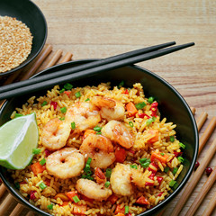 Wall Mural - Delicious fried rice with shrimps, lime and vegetables in a black bowl on a bamboo placemat. Traditional Asian food on a wooden table.