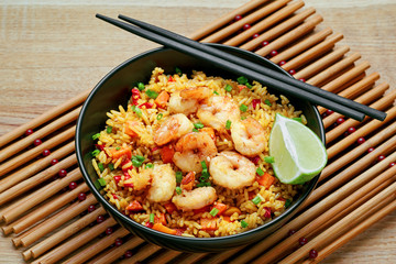 Wall Mural - Shrimp fried rice with vegetables, green onions and lime in a black pottery bowl on a bamboo placemat. Traditional Thai meal with sesame on a table.