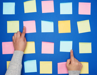 two female hands and a lot of empty paper multi-colored square stickers on a blue background