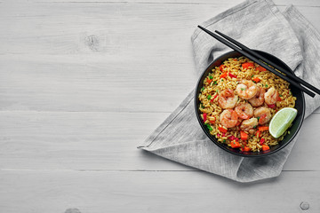 Shrimp fried rice with vegetables, green onions and lime in a black pottery bowl. Traditional Thai meal on a white table with fabric tablecloth. Top view, directly above shot with space for text.