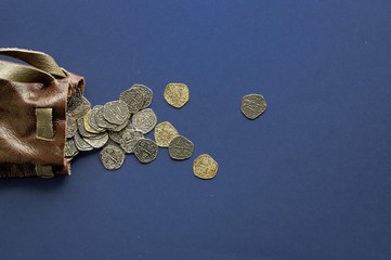 Sticker - Overhead shot of old coins spilled out of the bag on a dark blue surface