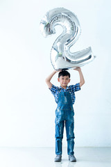 Asian happy boy with number 2 on white background, holding silver ballon number 2