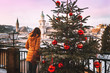 A young woman stands next to a beautiful Christmas tree with bright red balls and looks at the Salzburg Cathedral.Christmas trees with red Christmas balls against the background of the winter Salzburg