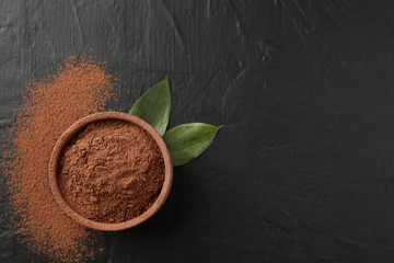 Bowl with cocoa powder and leaves on black background, space for text