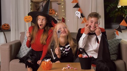 Sticker - halloween, holiday and childhood concept - smiling boy and girls in costumes with party props and having fun at home