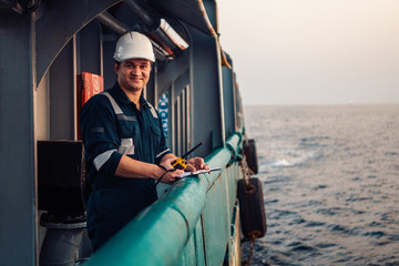 Deck Officer on deck of offshore vessel or ship , wearing PPE personal protective equipment. He fills checklist. Paperwork at sea