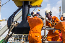 Offshore Workers Installing A Heavy Lifting Sling Onto A Crane Hook On Board A Construction Work Barge At Oil Field