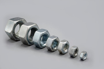 Metal nuts arranged in row on gray background. New and shiny chrome nuts. Copy space.