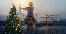 Asian Boy On Father's Shoulders Near Christmas Tree With Background Of New High Buildings And Silhouette Construction Cranes Of Evening Sunset, Father And Son On Christmas Time