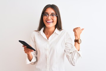 Wall Mural - Beautiful businesswoman wearing glasses using smartphone over isolated white background pointing and showing with thumb up to the side with happy face smiling