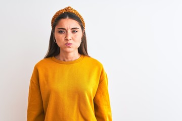 Wall Mural - Young beautiful woman wearing yellow sweater and diadem over isolated white background puffing cheeks with funny face. Mouth inflated with air, crazy expression.