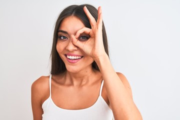 Wall Mural - Young beautiful woman wearing casual t-shirt standing over isolated white background with happy face smiling doing ok sign with hand on eye looking through fingers