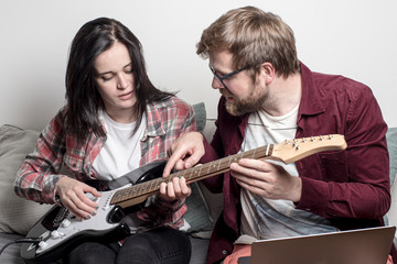 man teaches a woman to play a six-string electric guitar.